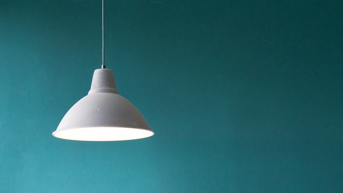 A white pendant light glowing against a teal wall